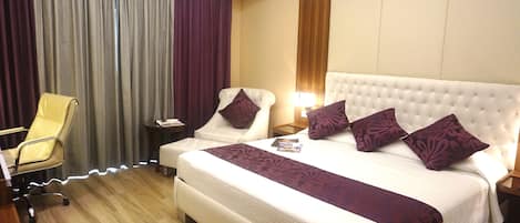 Una habitación de hotel con una cama grande, dos mesitas de noche, una silla y un escritorio.