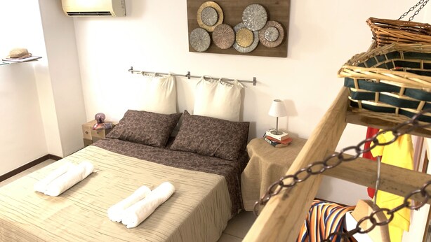 A neatly made bed with white towels, a wall-mounted air conditioner, a decorative wall piece, and a small bedside table with a lamp. - Azzurra Flat Bari Center (Bari)