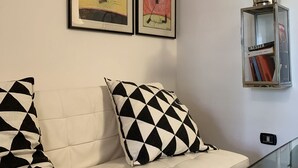 A white sofa with black and white patterned pillows, two framed artworks, a yellow 'Smile' sign, and a metal lantern with books. - Azzurra Flat Bari Center (Bari)