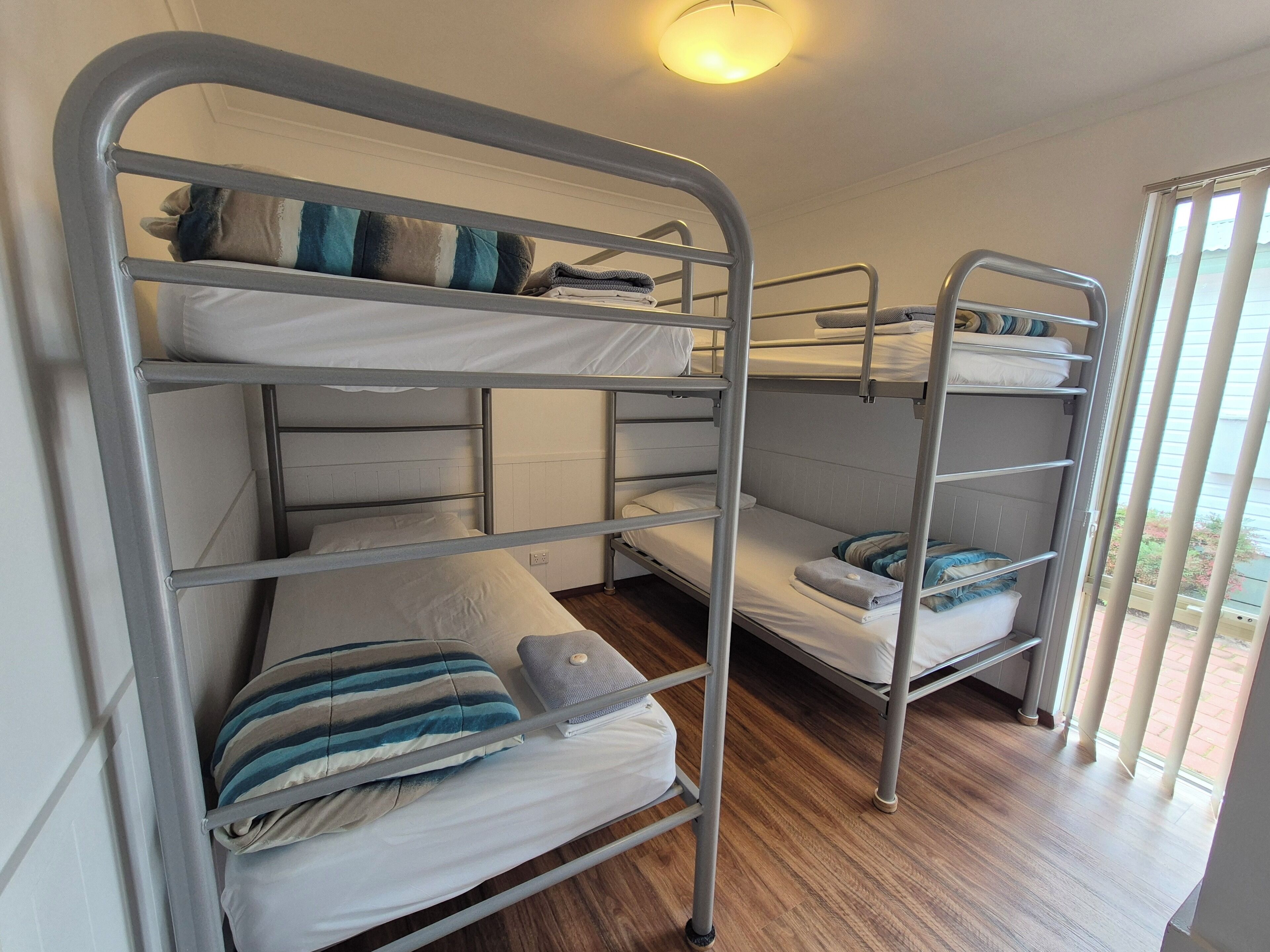 Habitación con literas de metal, ropa de cama blanca y suelo de madera.