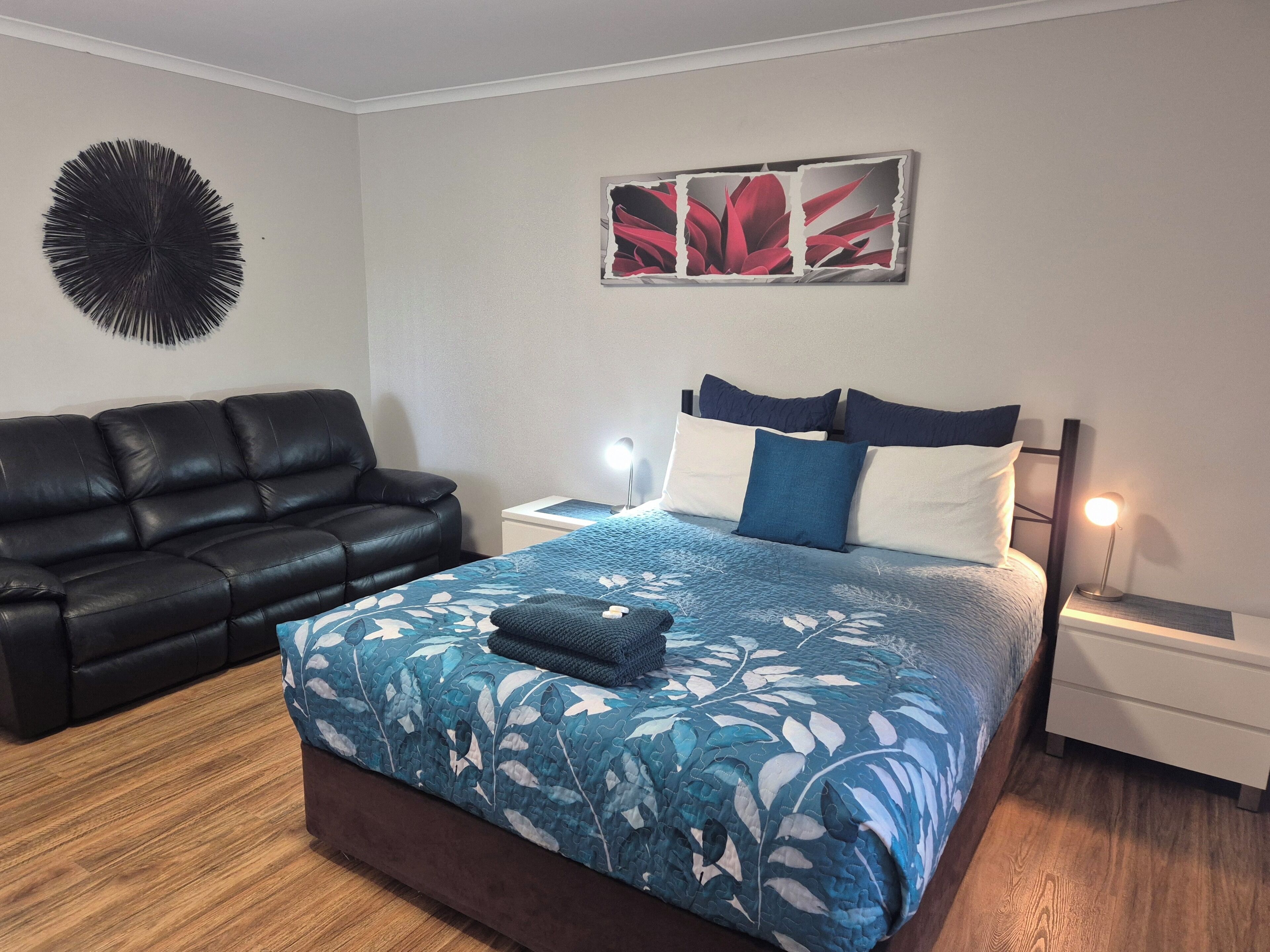 Une chambre à coucher comprenant un lit, un canapé en cuir noir, une table de chevet avec une lampe et une œuvre d’art murale.