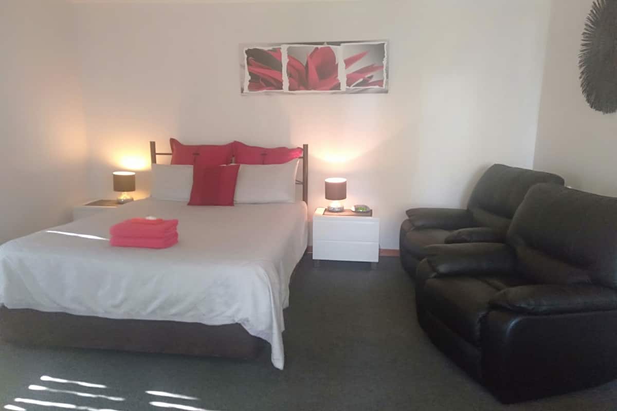 A hotel room with a bed, two bedside tables, a nightstand, a leather sofa, and a wall-mounted artwork.