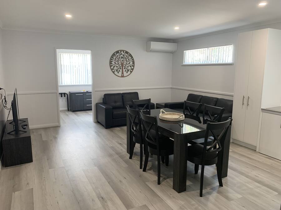 Een moderne woonkamer met een eethoek, met een zwarte leren bank, een glazen eettafel en een decoratief wandobject.