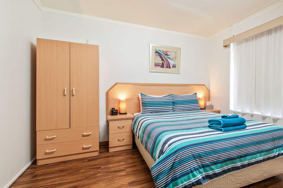 A bedroom with a bed, a wardrobe, a nightstand, a lamp, and a window with curtains.