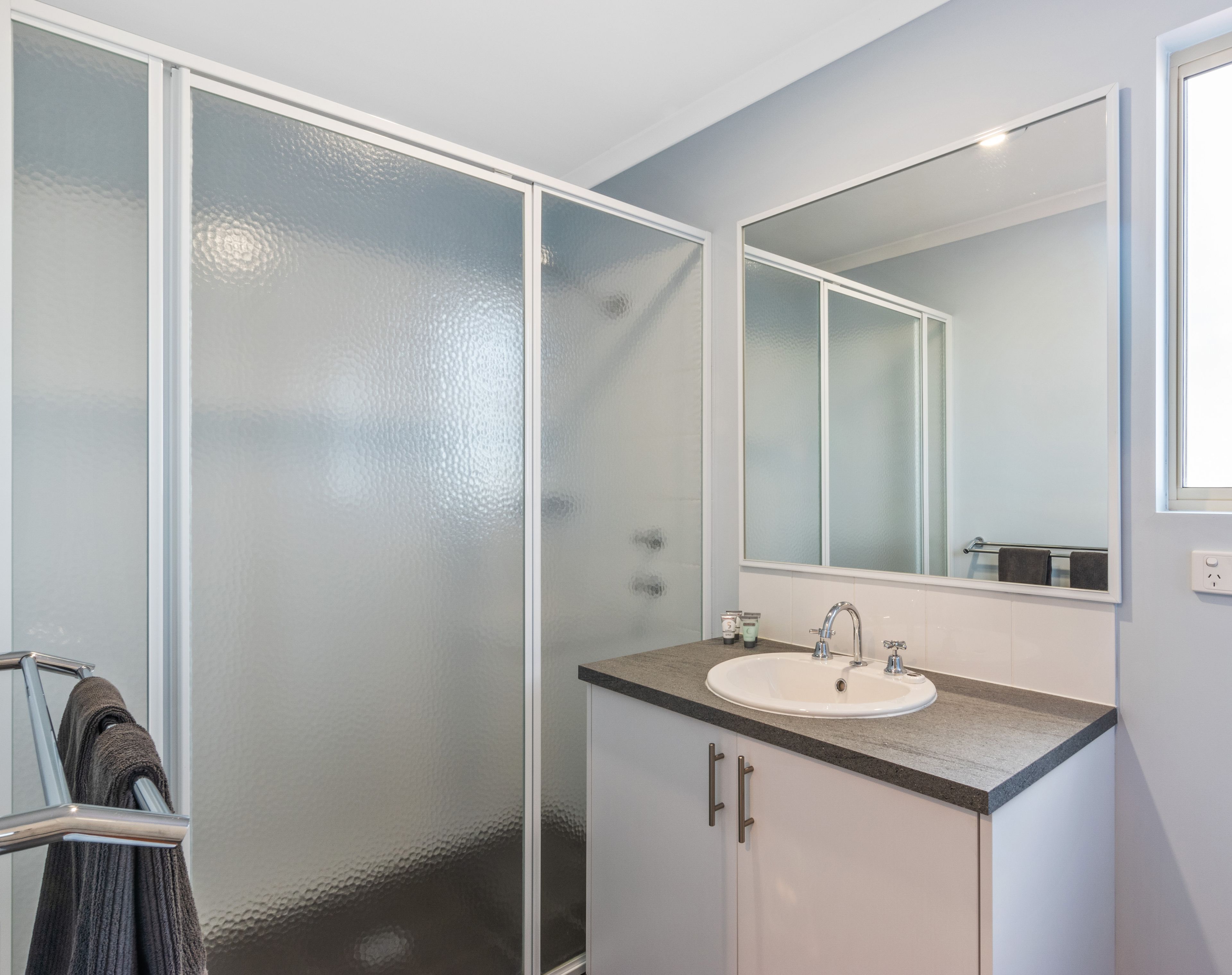 Une salle de bain avec une douche à parois de verre, un lavabo avec un miroir au-dessus et un porte-serviettes avec une serviette.