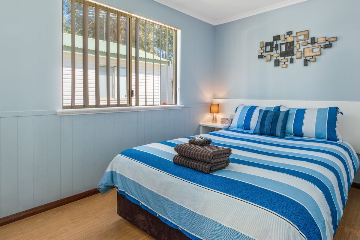 A bedroom with a bed, a nightstand, a lamp, a window, and a wall decoration.