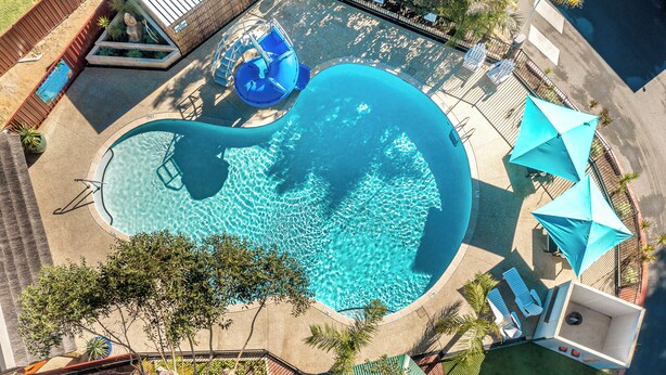 An aerial view of a swimming pool with a slide, lounge chairs, and umbrellas. - Mandurah Caravan & Tourist Park (Furnissdale)
