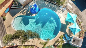 Vue aérienne d’une piscine avec un toboggan, des chaises longues et des parasols.
