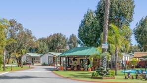 A reception area with a green roof, a sign indicating 'Reception', and a pool with lounge chairs. - Mandurah Caravan & Tourist Park (Furnissdale)