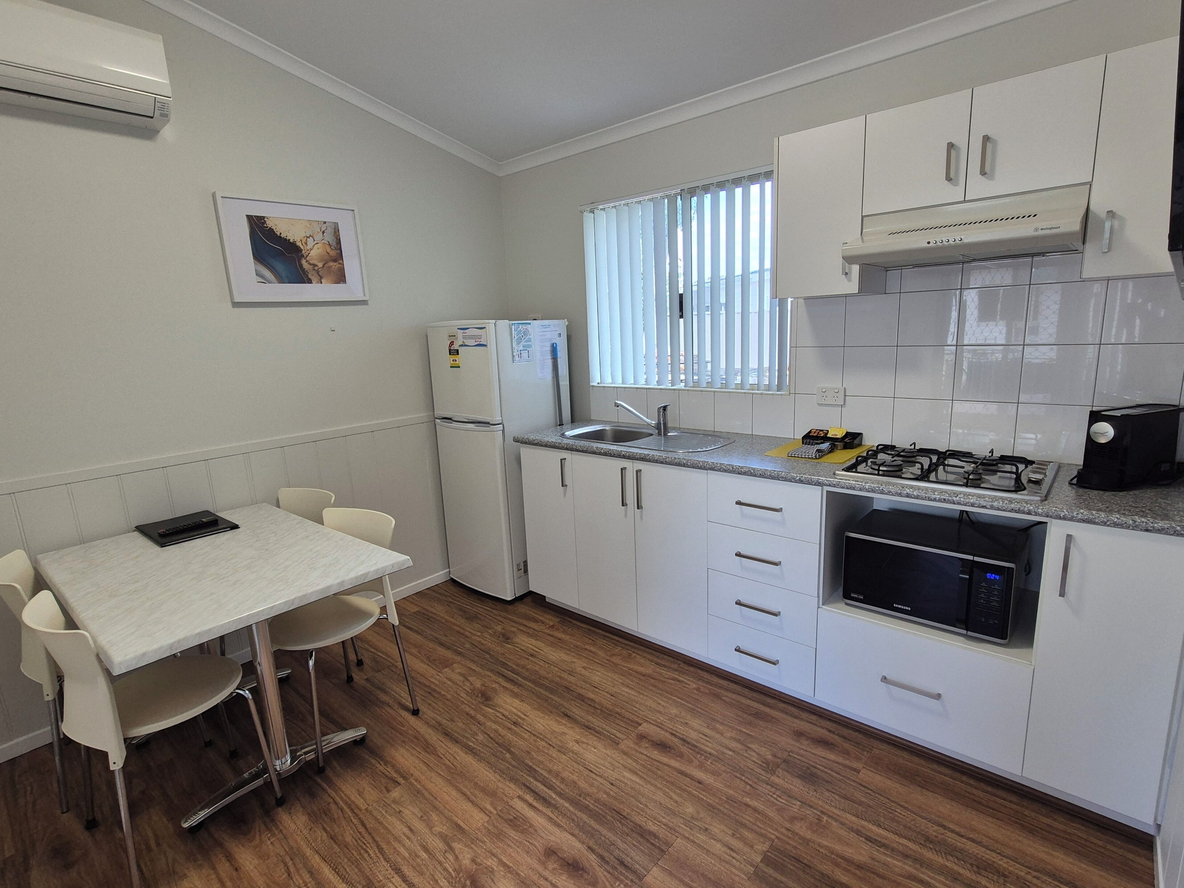 A compact kitchen with white cabinets, a gas stove, a refrigerator, and a dining area with a table and chairs.