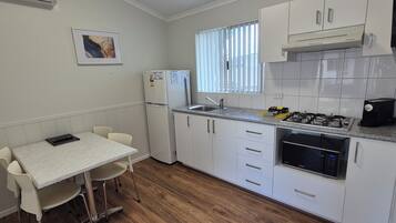 A compact kitchen with white cabinets, a gas stove, a refrigerator, and a dining area with a table and chairs.