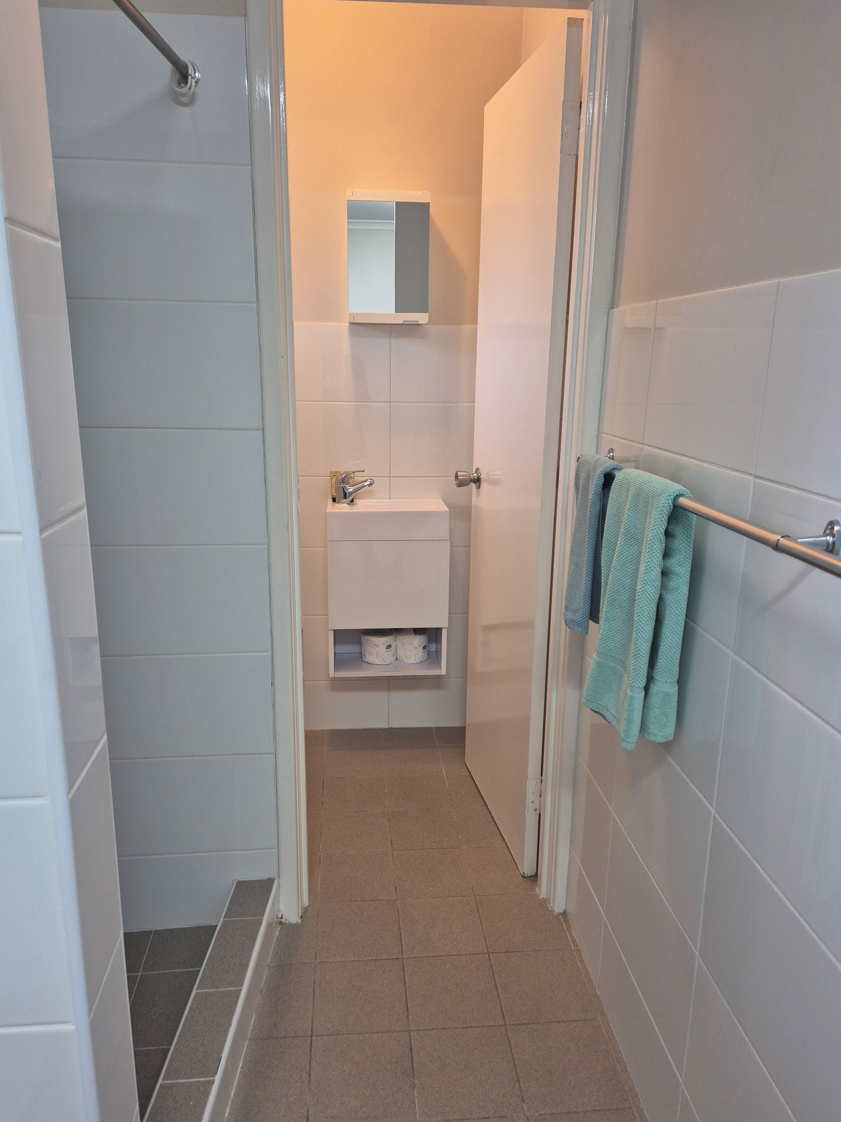A narrow bathroom with a shower, toilet, and sink.