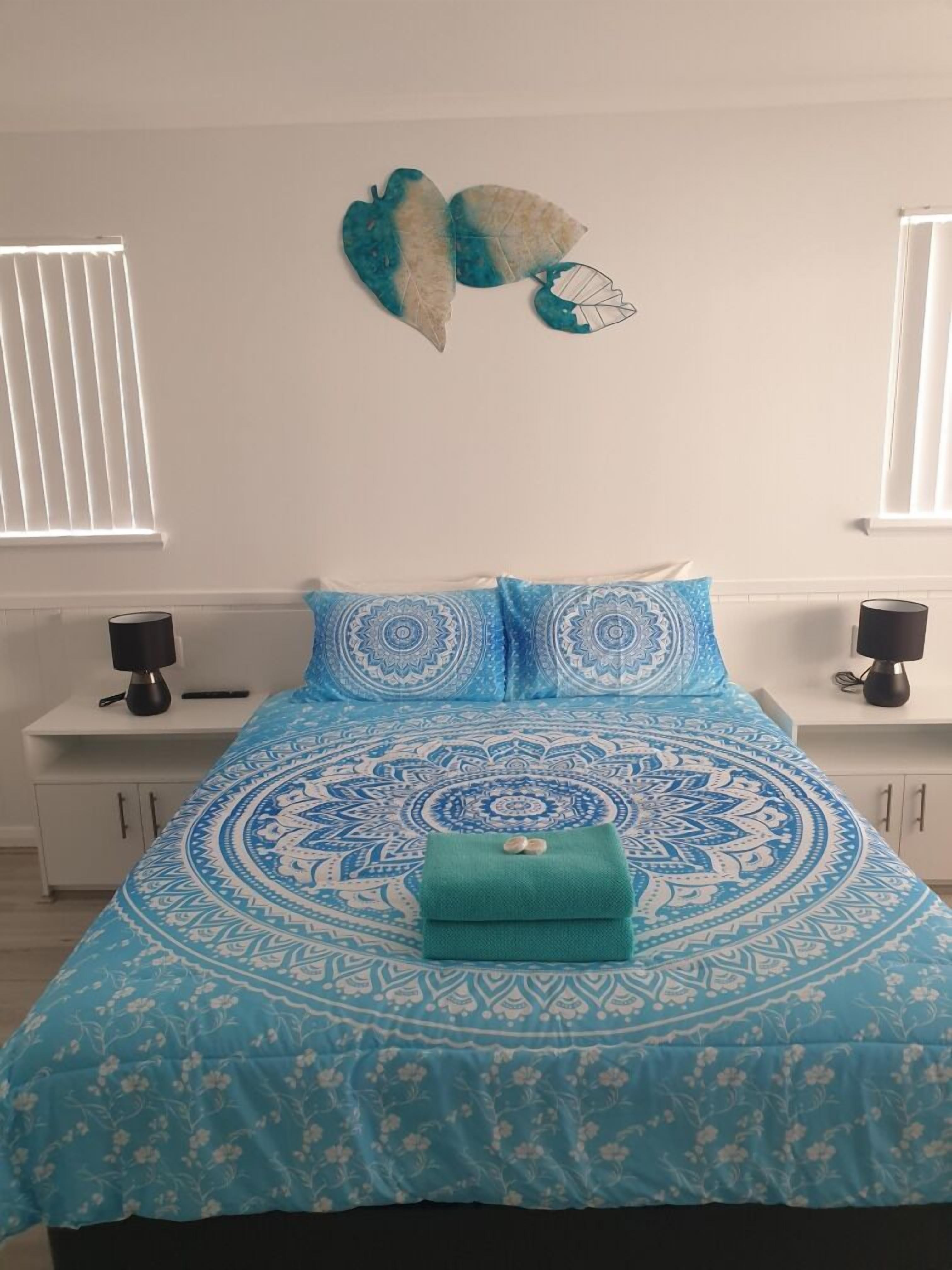 A bedroom with a blue patterned bedspread, two matching pillows, a teal throw, and a wall-mounted decorative piece.