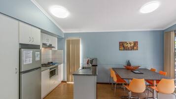A compact kitchen with a dining area, featuring a refrigerator, oven, and a small island with a sink.