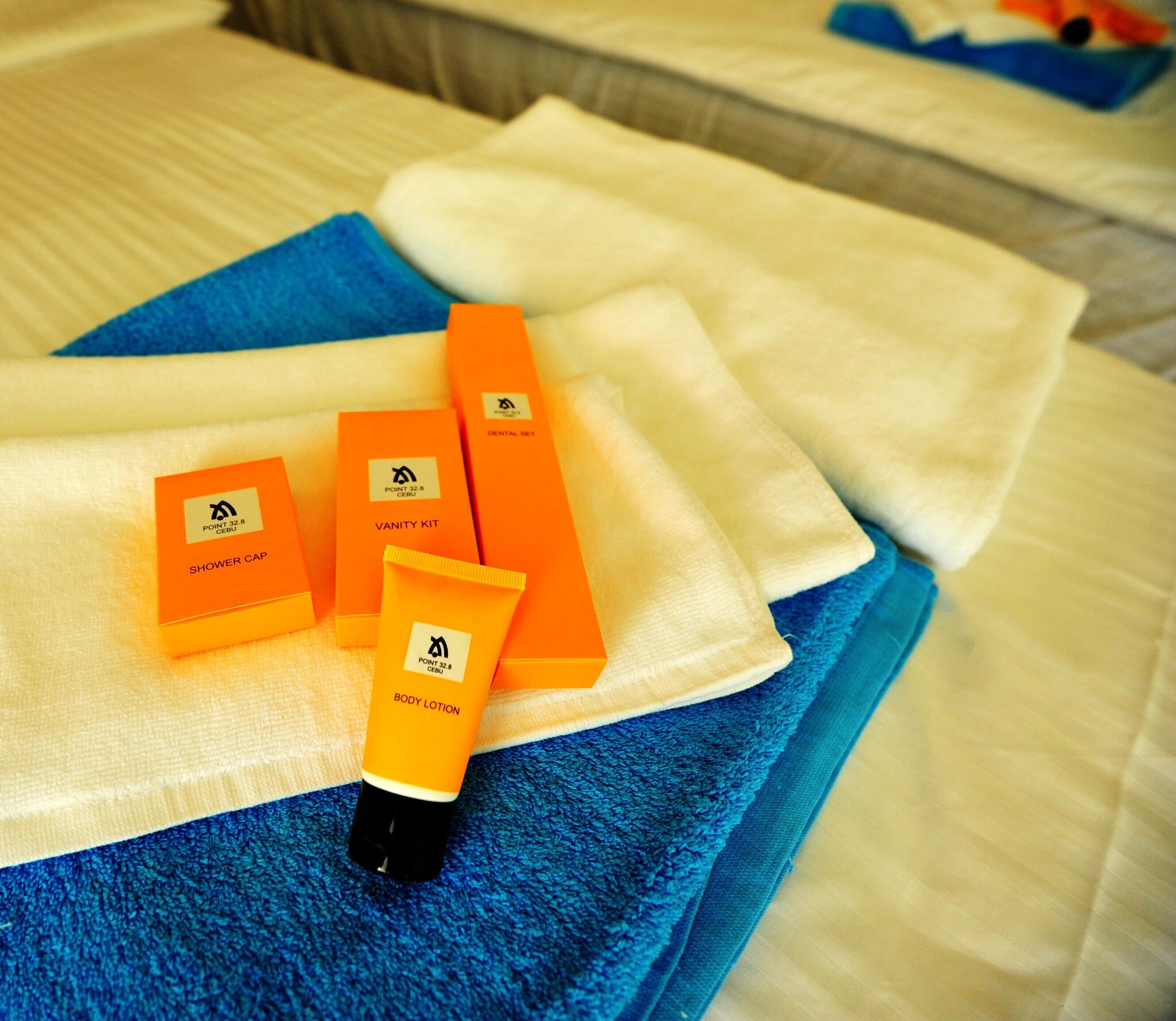Une salle de bain avec une serviette bleue, un tapis de bain blanc et des articles de toilette, notamment un bonnet de douche, une trousse de toilette et une lotion pour le corps.