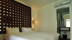 Una habitación de hotel con una cama grande, cabecero de madera, luz empotrada en la pared y un baño con lavamanos y espejo.