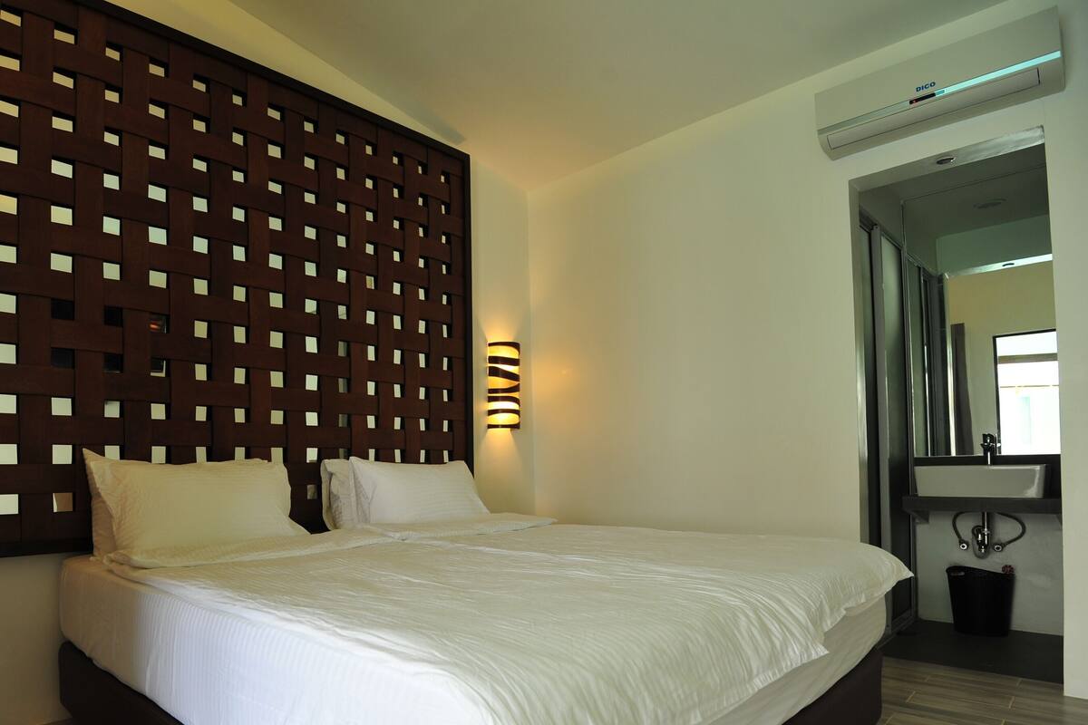 Hotelkamer met een groot bed, een houten hoofdbord, een wandlamp en een badkamer met een wastafel en spiegel.