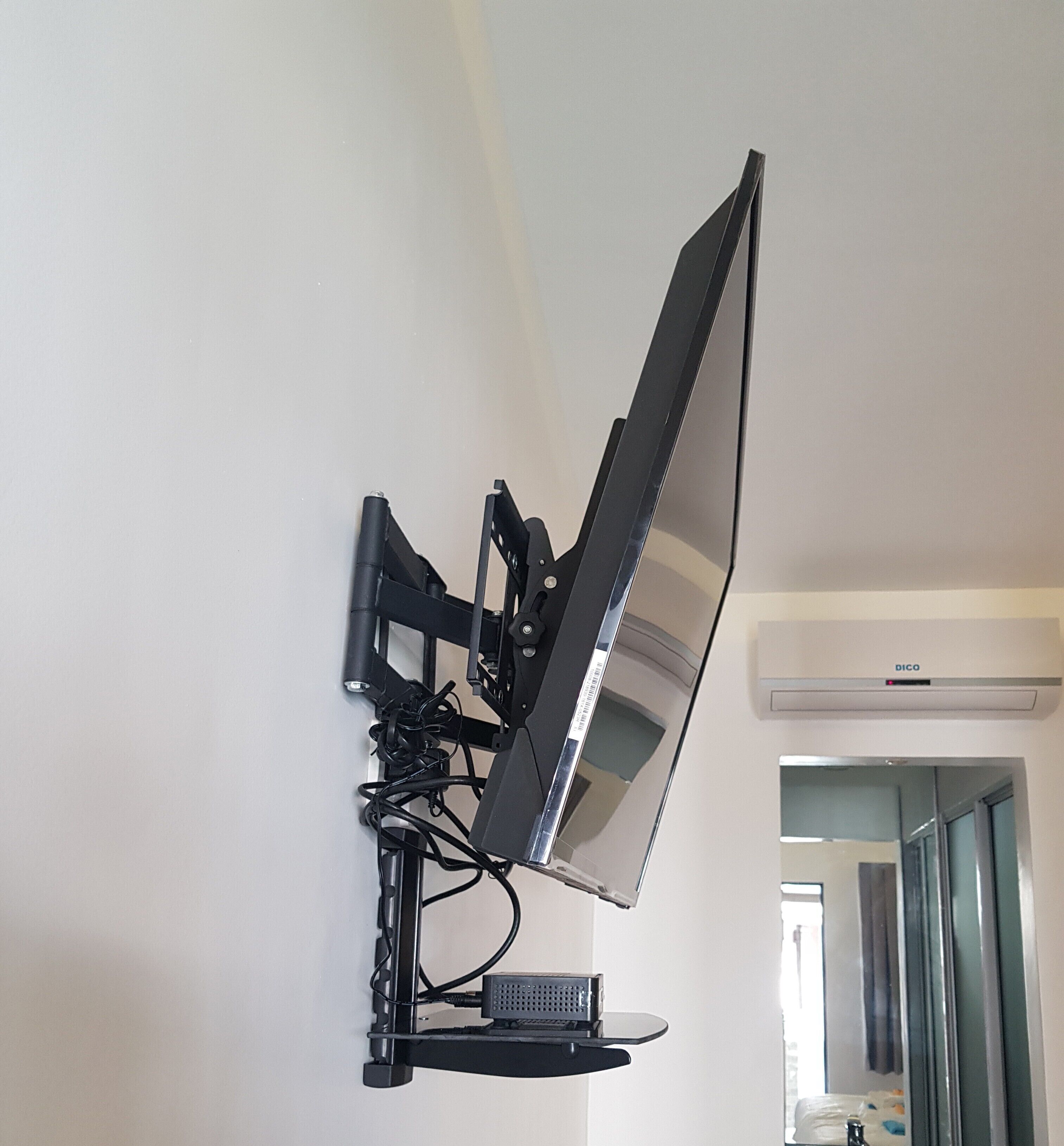 A wall-mounted television with a stand, cables, and a remote control.