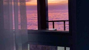 Una habitación con vistas a la puesta de sol sobre el océano, una ventana con lámpara y una pared de ladrillo.