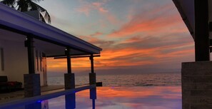 Sonnenuntergangblick von einer überdachten Außenanlage mit Pool, mit Blick auf den Ozean.