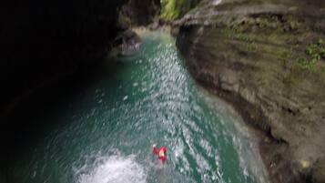 A person in a red jacket swimming in a river surrounded by rocky cliffs.