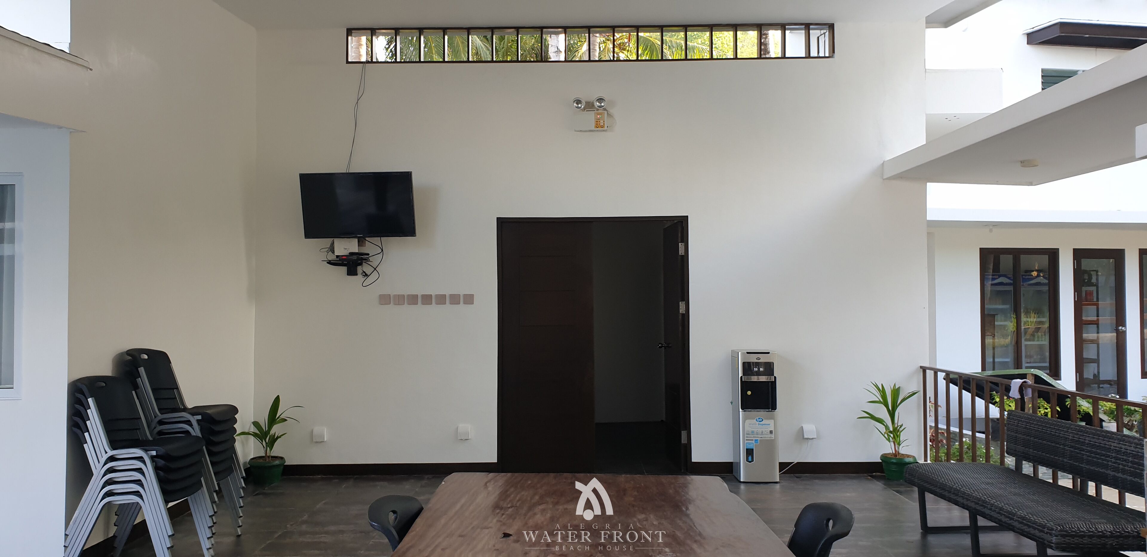 A conference room with a large table, chairs, a TV, a water dispenser, and a door.