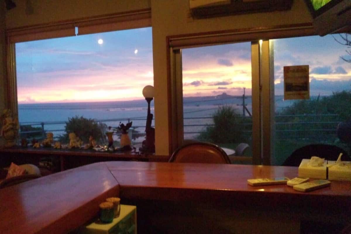 Un restaurante con vistas a la puesta de sol sobre el océano, una zona de bar y una disposición de mesas y sillas.
