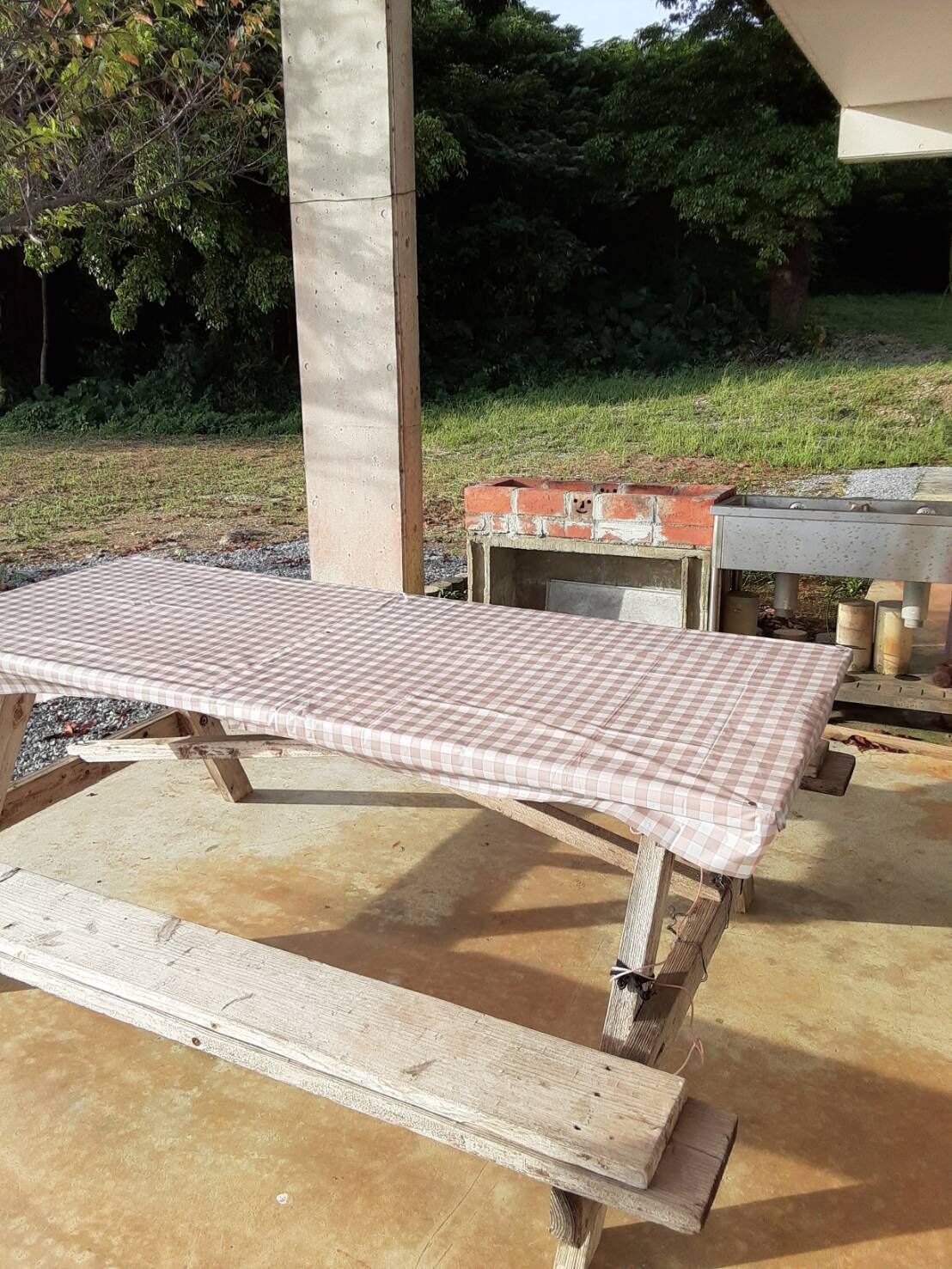A concrete pillar, a checkered table, and a brick oven in an outdoor setting.