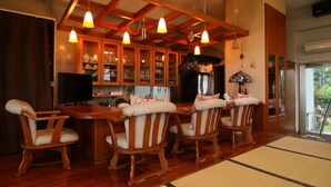 A dining area with wooden chairs and a table, wooden cabinets with glass doors, and pendant lights. - Minshuku Tantawan (Motobu)