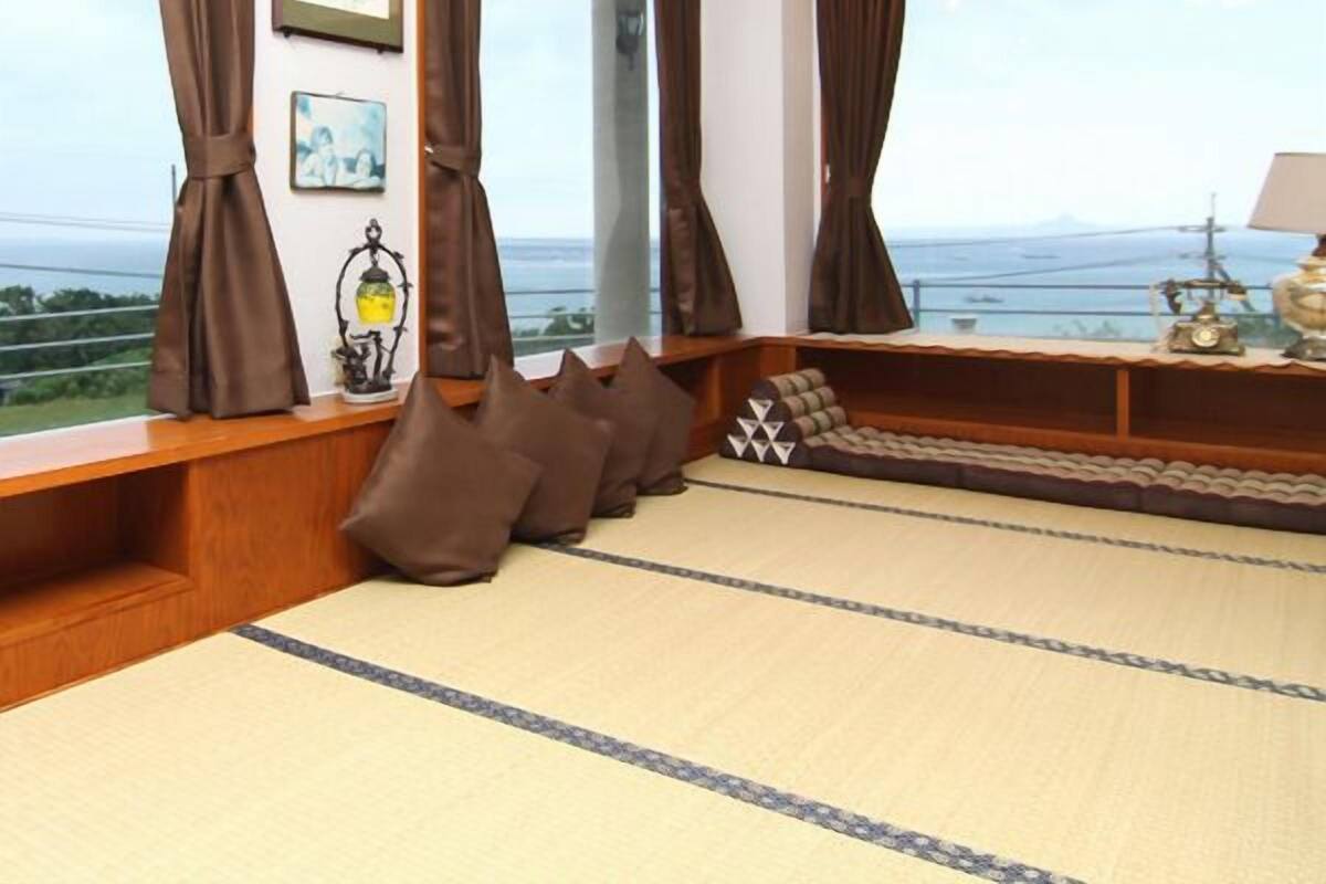 Quarto com amplas janelas, um banco de madeira e vista para o mar.