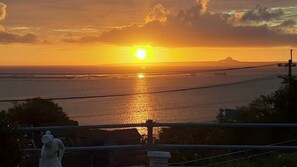 A sunset over a body of water with a statue in the foreground. - Minshuku Tantawan (Motobu)