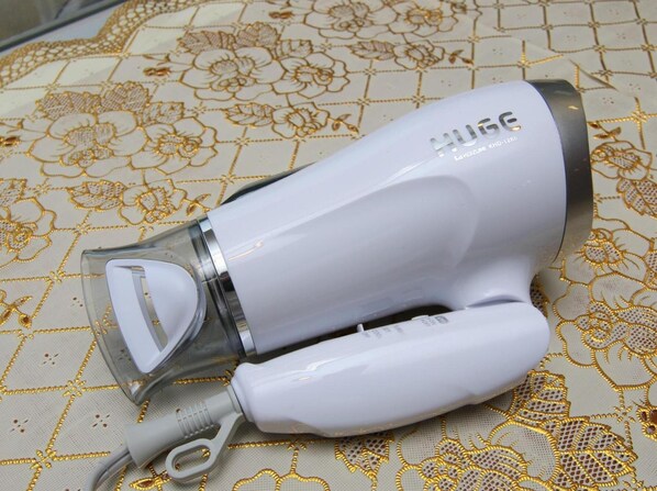 A white hairdryer with a transparent water bottle attached, lying on a patterned fabric surface.