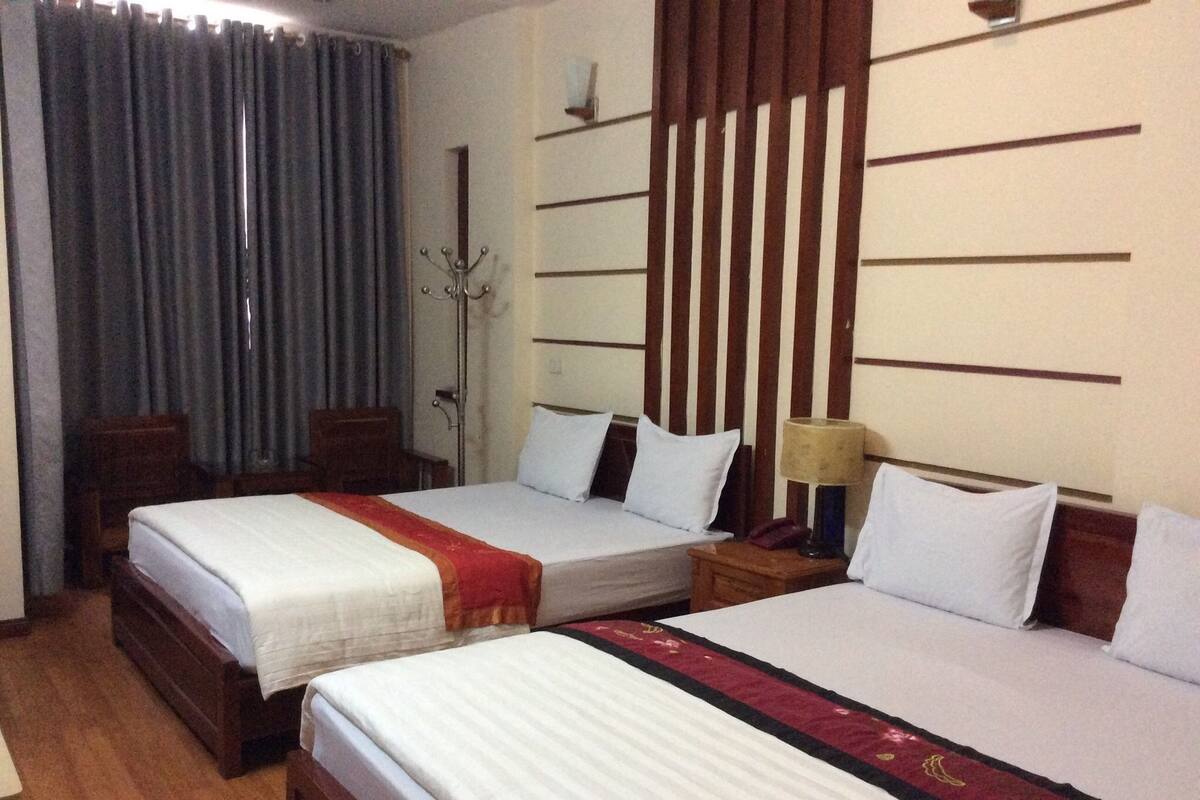 A hotel room with two beds, a wooden headboard, a nightstand with a lamp, and a chair.