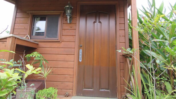 A wooden house with a front door, a small window, and a porch with plants. - Yambarunomori (Ogimi)