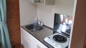 A compact kitchenette with a sink, a stove, and a small shelf above the sink. - Yambarunomori (Ogimi)