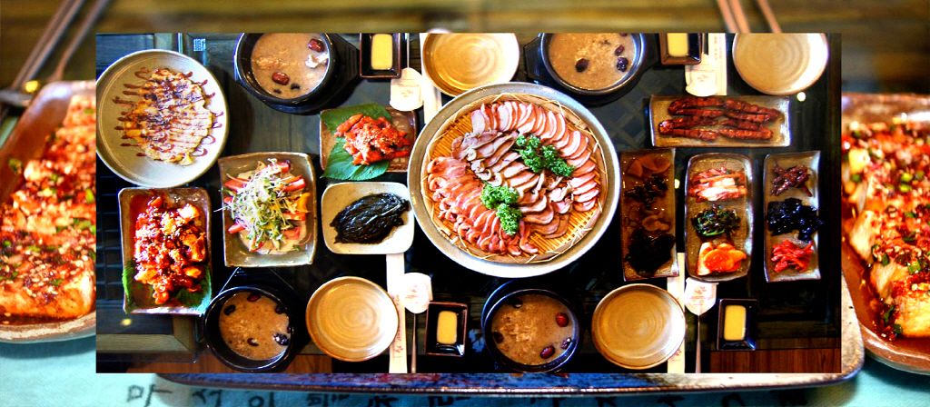 A variety of dishes arranged on a table, including a large platter of sliced meats, bowls of soup, and other food items.