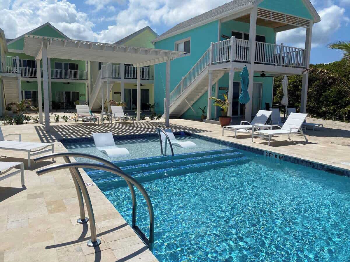 A swimming pool with a 3 ft 8 in depth, surrounded by lounge chairs and a covered area with stairs leading to a balcony.