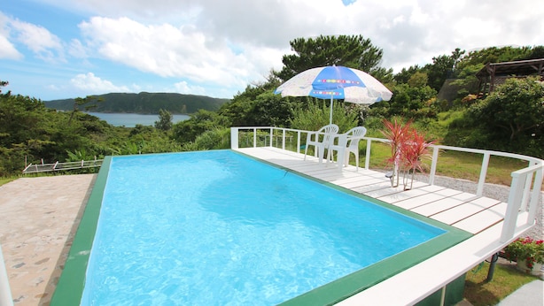 Piscina rectangular con una terraza blanca y una sombrilla azul.