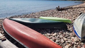 Kajakker på række ved en rolig sø med en stenet strand.