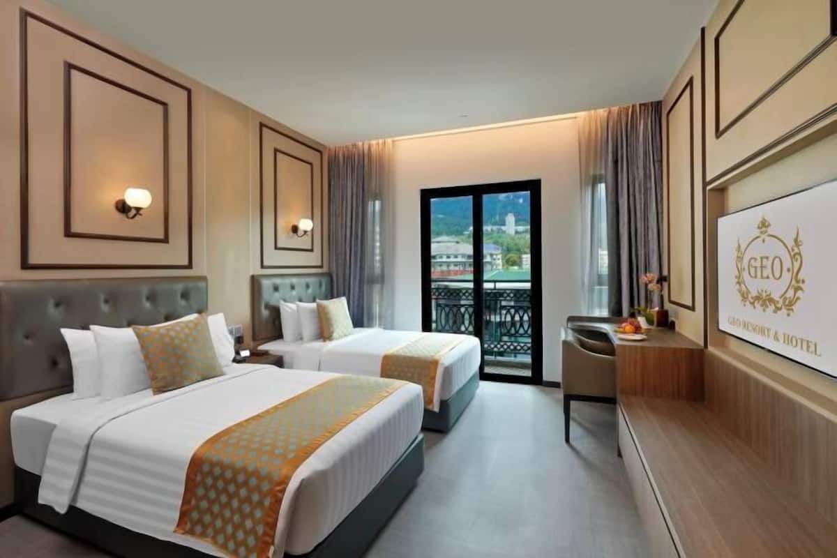 A hotel room with two beds, a desk, a TV, and a balcony with a city view.