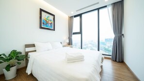 A modern hotel room with a large bed, a potted plant, a nightstand, and a window with a city view. - Jaan Apartment 29 Lieu Giai (Hanoi)