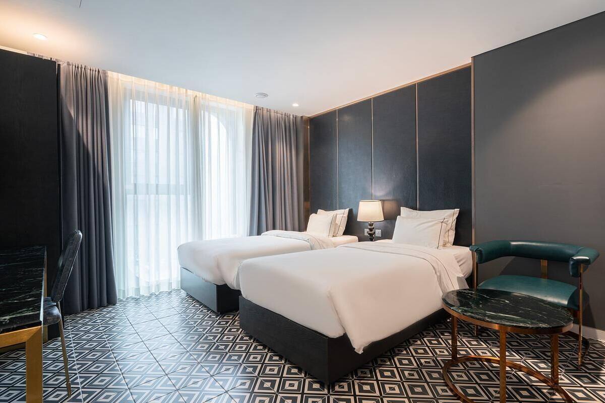 A hotel room with two beds, a desk, a chair, and a large window with curtains.