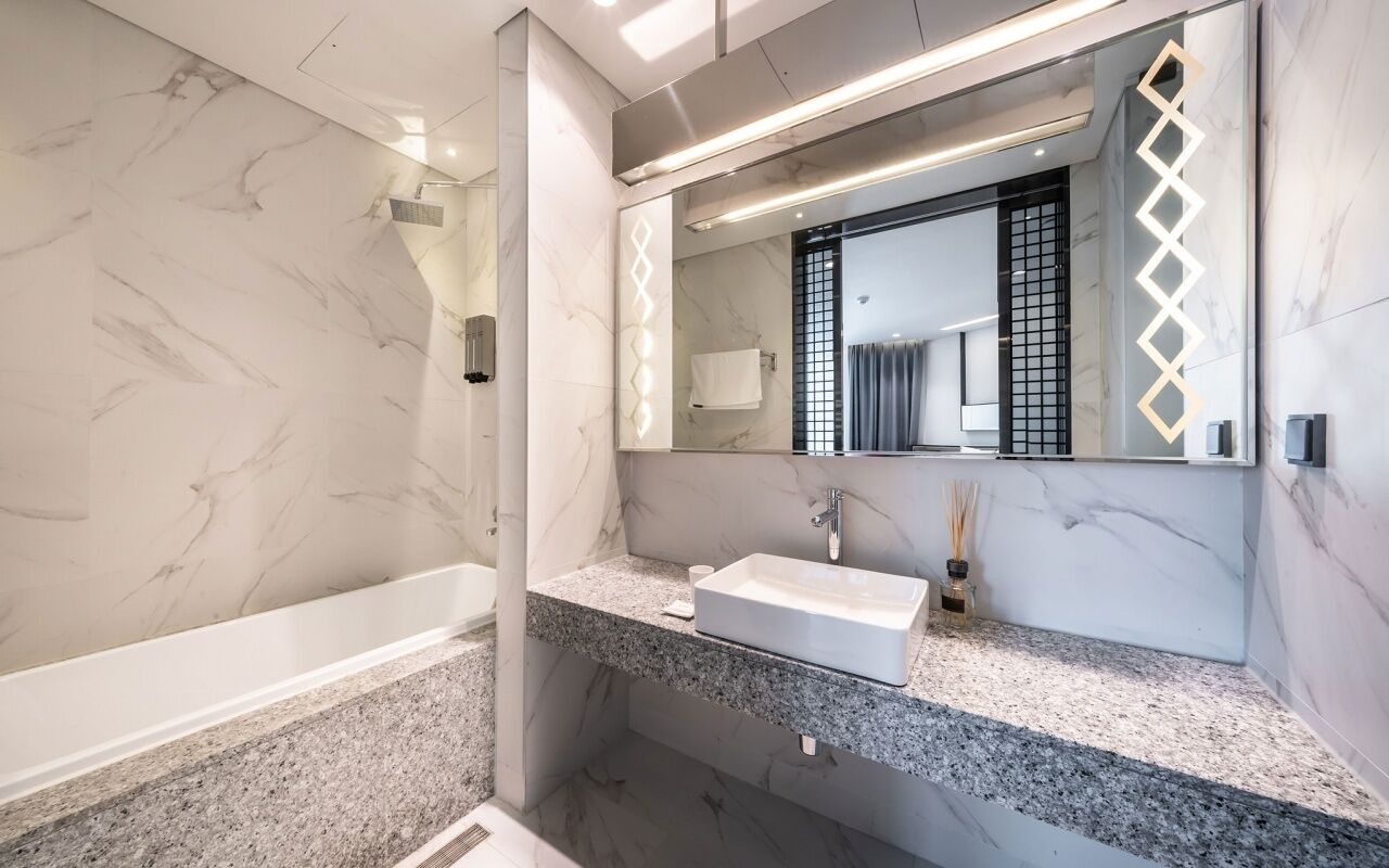 A modern bathroom with a marble floor, a freestanding bathtub, a large mirror, and a granite countertop.