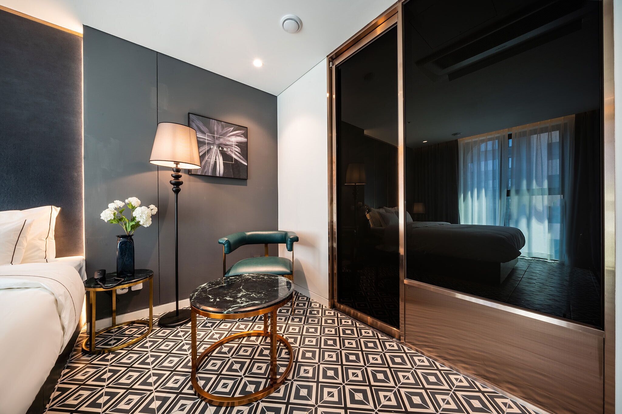 Une chambre d’hôtel moderne, équipée d’un lit, d’un bureau avec une lampe, d’une chaise et d’une grande fenêtre avec des rideaux.