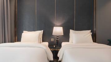 A hotel room with two beds, a round table with a lamp, and a dark wall with vertical lines.