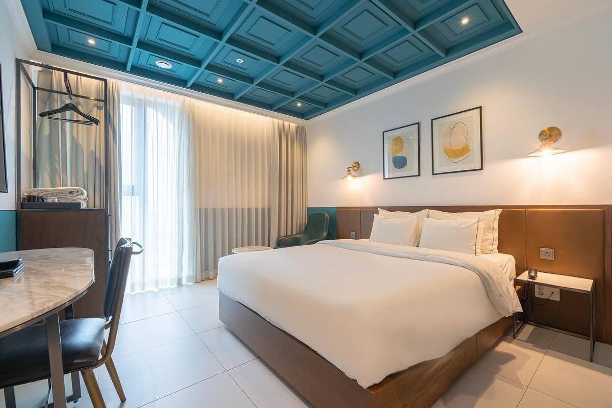 A hotel room with a bed, bedside table, chair, and a desk with a chair.