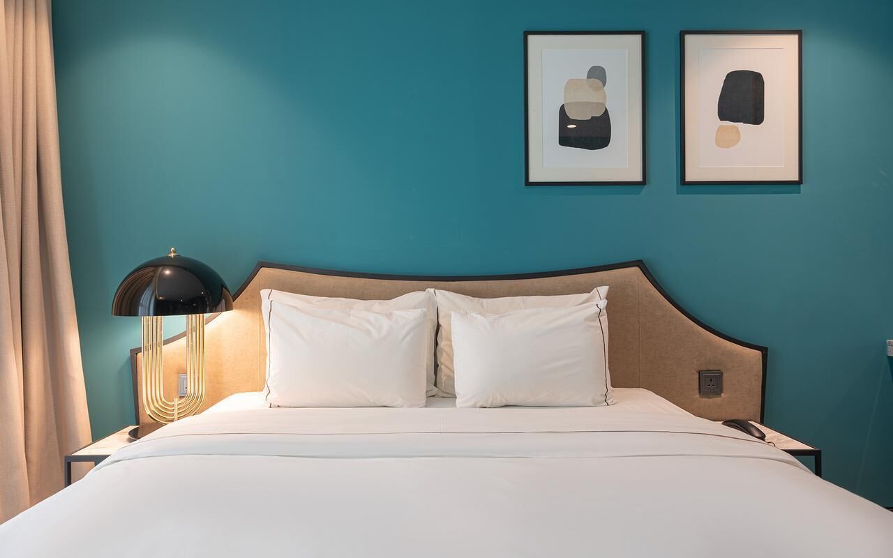 A hotel room with a bed, a nightstand, a lamp, and two framed artworks on the wall.