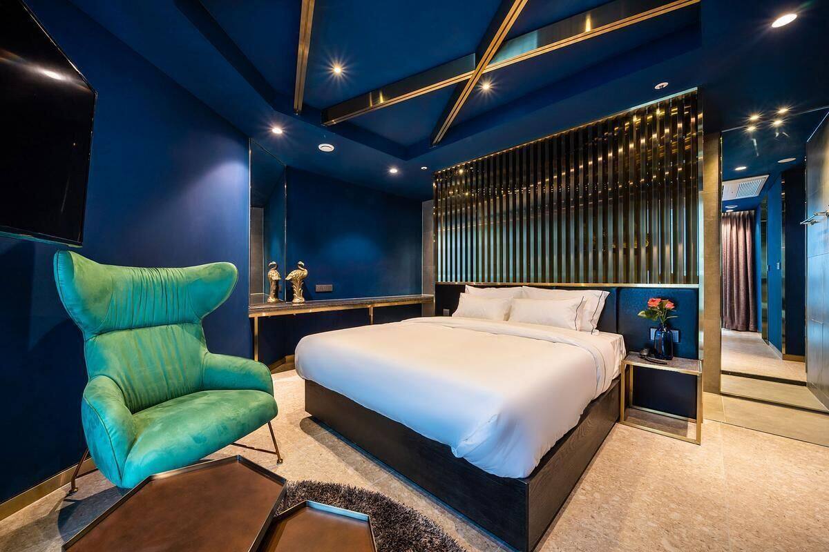 A modern bedroom with a large bed, a green armchair, and a TV mounted on the wall.
