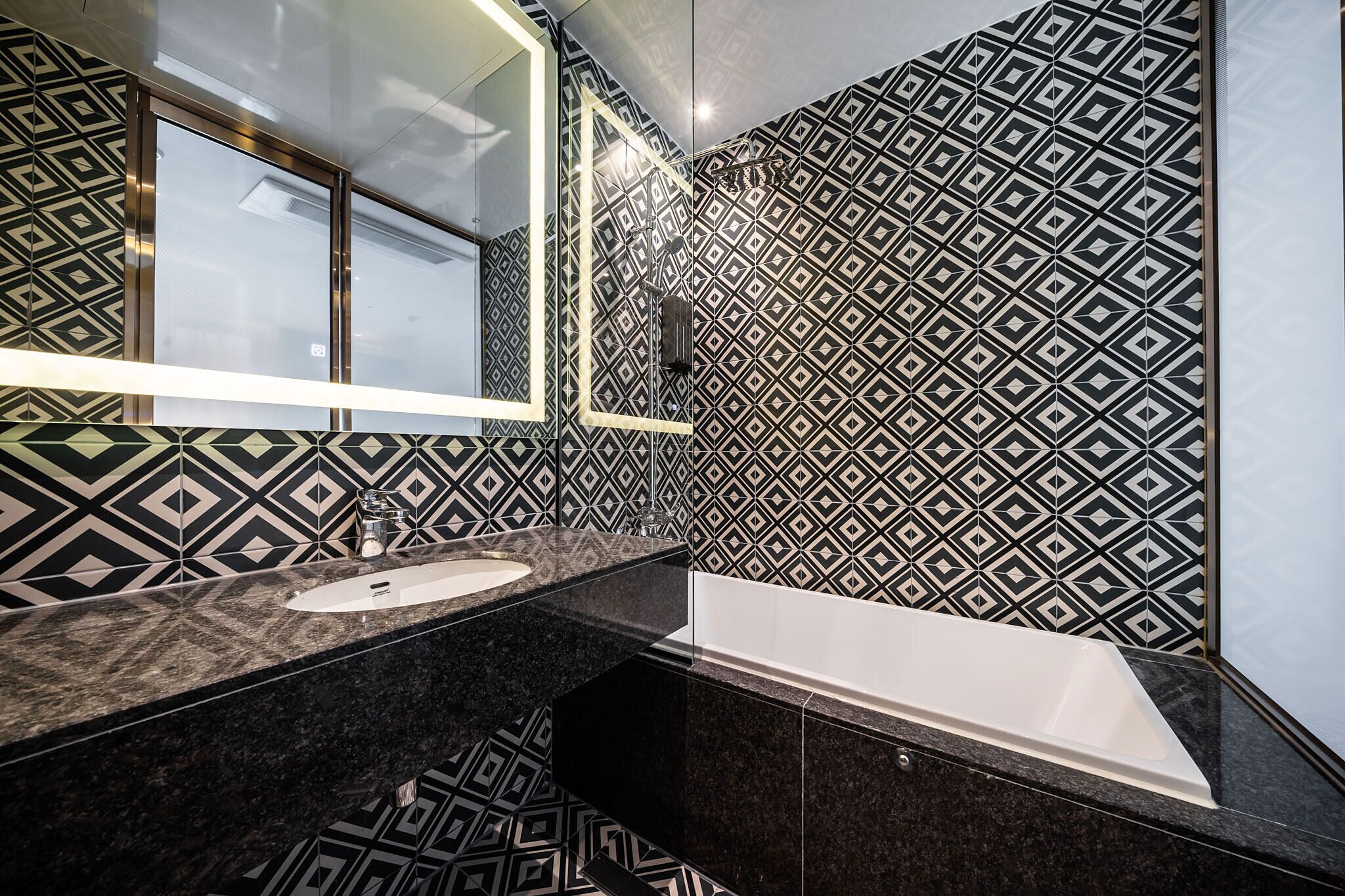 Un baño moderno con pared de patrón geométrico, un lavamanos blanco y una bañera independiente.