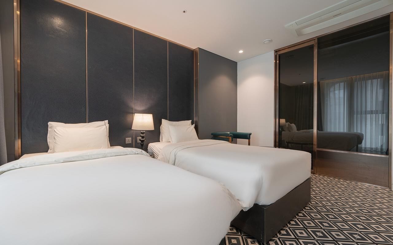 A hotel room with two beds, a desk, a chair, and a large mirror.